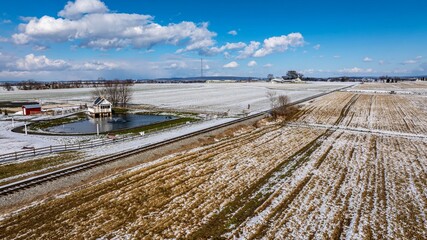 An Aerial View Of A Rural Landscape With A Pond House And Snow-Covered Fields.