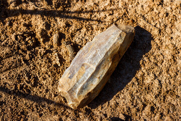An ancient flint tool covered with a whitish patina lying on the ground, a Stone Age artifact at...