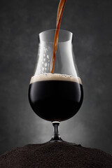 Stream of dark stout pours into a beer glass. Beer with dark beer on a black sand and dark...