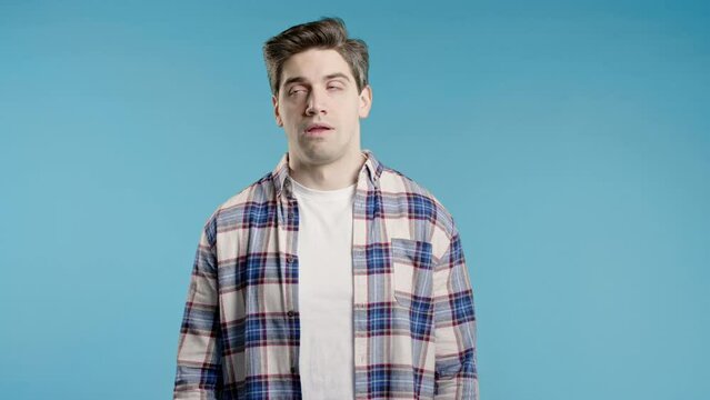 Bored upset man sighs, rolling eyes on blue backdrop. Irritated dude displeasure