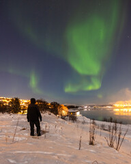 A man watches the Northern Lights over the Norwegian City of Tromso