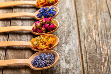 Assortment of dry herbal and berry tea in wooden spoons on a wooden background.Medicinal Healing herbs.Alternative medicine concept.Linden, calendula, cornflowers, marigold, tansy, tea rose.dry herbal