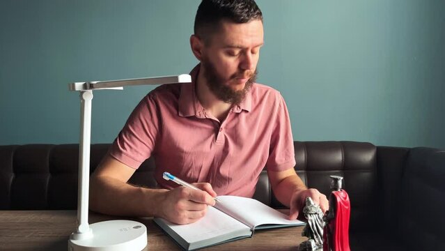 A man looks out the window and writes something