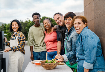 Happy multigenerational friends having fun preparing food at house rooftop - Diversity people...