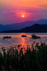 Tranquil Sunset Over Lake Garda with Boats and Mountain Silhouettes