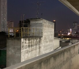 Obraz premium Night blur photo of rooftop on old building in Bangkok, Thailand with high sky building as background, deck with exit door and fence