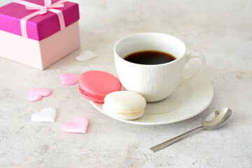 a cup of coffee and cookies with a pink box of macaroons 