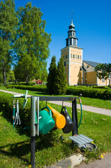 Garden care tools watering cans, shovel, rakes in the graveyard by the yellow and white church building of Ramnäs church in Sweden on spring sunny day