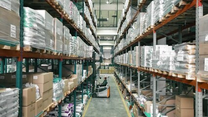 Organized warehouse aisles, An employee of the logistics warehouse puts the cargo on the shelf with a forklift - Powered by Adobe