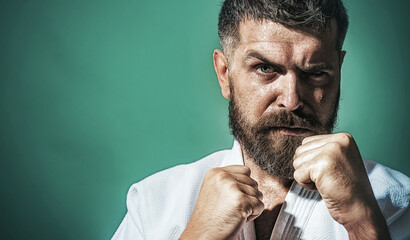 Serious bearded man in kimono in fighting position. Karate fighter preparing for competition. Muscular male ready for karate training. Strong martial arts master on fight. Copy space for advertising.
