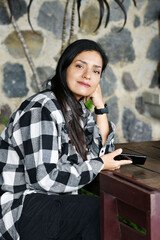 Mujer bonita sentada en una silla de madera sosteniendo su teléfono móvil con la mano.