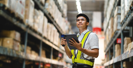 A man wearing a yellow vest and safety glasses is holding a tablet in a warehouse. He is smiling...