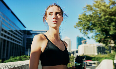 Woman, thinking and water outdoors in city for rest, fitness and wellness in sportswear by buildings. Break, runner and workout in urban town for breathing, goals and challenge for cardio in new york