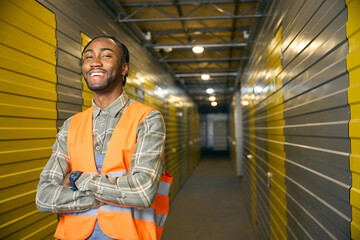 Cheerful worker in reflective vest posing for camera in storehouse