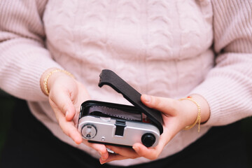 Girl in a pink sweater putting film on a photo camera.