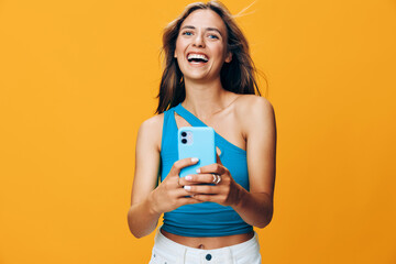 Beautiful young woman smiling and holding a smartphone against a bright orange background