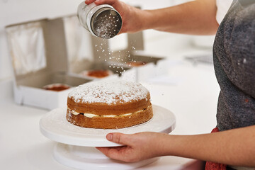 Cake, person and hands with icing sugar on table for small business, preparation and confectionery....