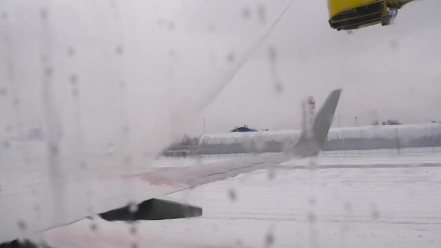 View of de-icing a plane wing process from airplane window. Winter frosty day at airport