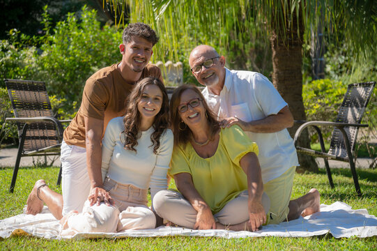 Fam&iacute;lia feliz sentada no jardim em dia ensolarada, Irm&atilde;os com suas esposa no jardim em meio a natureza, casal se divertindo em fam&iacute;lia