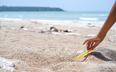 Woman hands pick up yellow plastic tube left on the sandy beach, Cleaning the beach, Collecting trash at the beach. Environmental Conservation concept.