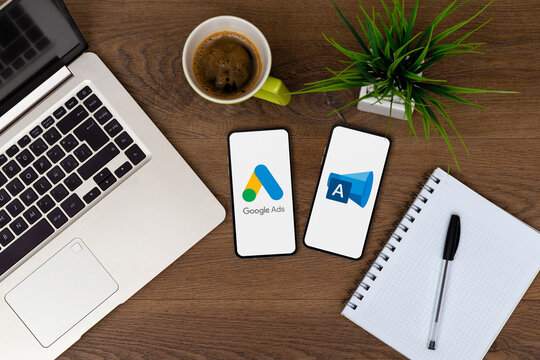 Google Ads and Microsoft Ads apps in a two smartphones over a desk. Top view in a flat lay photo of both mobile phones next to a laptop, a coffee cup and a notepad.