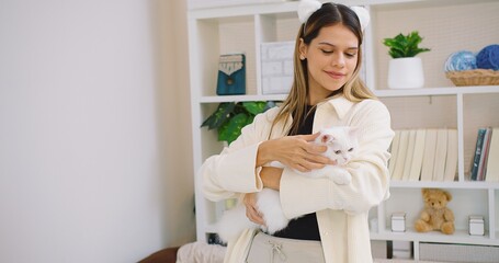 Cute pretty young beautiful woman is holding hugging embrace cute little fluffy a white cat in her...