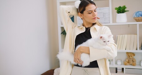 Cute pretty young beautiful woman is holding hugging embrace cute little fluffy a white cat in her...