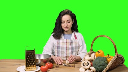 Young woman in apron cutting the mushrooms on the chroma key