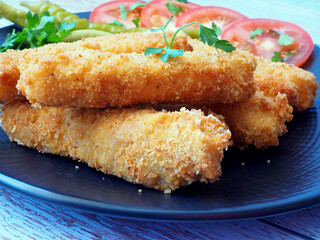 Close-up of Fried Fish Sticks with Fresh Vegetables on a Black Plate