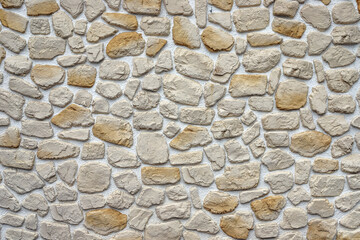 Decorative stone wall made of natural rocks of different colors and shapes plastered with white mortar as a background