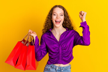 Photo portrait of lovely young lady hold shopping bags winning dressed stylish violet garment isolated on yellow color background