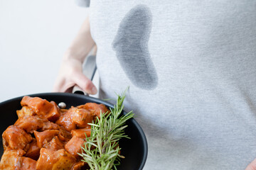 Splashing grease stain on gray clothes. An unrecognizable woman a frying pan with meat and herbs....