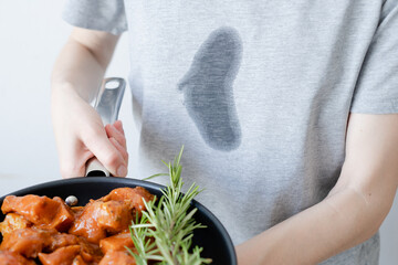 Dirty grease stain on clothes. An unrecognizable woman a frying pan with meat and herb. Cooking in...