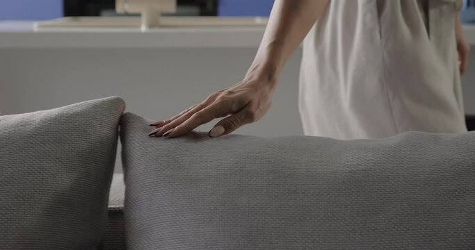 Woman hand touch pillow on sofa in living room. Young female hands gently touch grey pillow. Cozy minimalist living room
