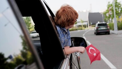 Kid looking out the car window while showing Turkey flag. Trip, lifestyle concept.