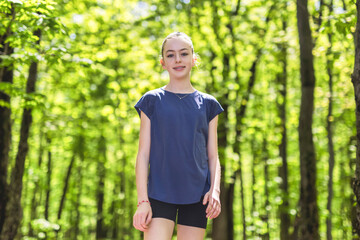 Fit child girl jogging in green park on a sunny summer evening.