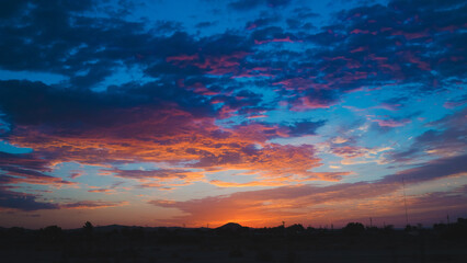 Colorful vibrant desert clouds at sunrise with silhouette of landscape horizon
