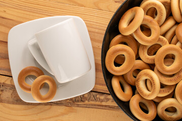 Several tasty bagels in a black ceramic plate with a white cup and saucer on a wooden table,...