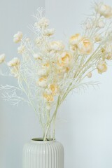 a white vase with dried flowers stands on a shelf