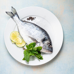 Raw fish dorada with lime slices, seasoning, and mint herb ready for cooking, directly above