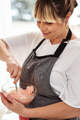 Woman, kitchen and icing for dessert, home and glass bowl for baking or small business. Baker, ingredients and mixing with spoon, house or startup bakery for recipe prepare and sweet food process