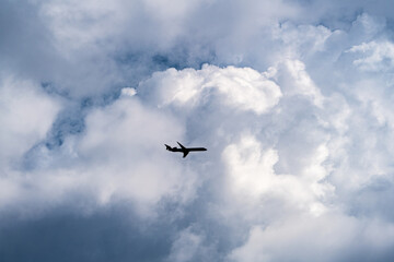 Looking up to the silhouette of a airplane in front of the spectacular big white clouds