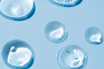 Round drops of transparent serum gel on blue background.