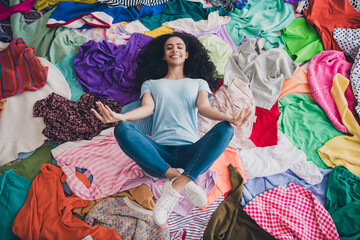 Above view full length photo of nice young girl lying meditate messy clutter clothes flat indoors