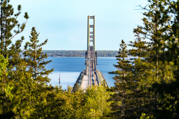 Mackinac Bridge through trees with blue sky and water showing traffic on bridge