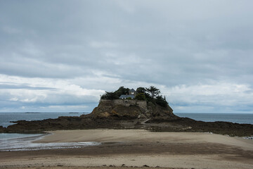 Fototapeta premium sandy beach with cliff and a house on it in the Baye of Le Mont Saint Michel in Bretagne with a clouded sky