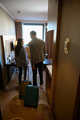Couple with wheeled baggage entering hotel room in morning