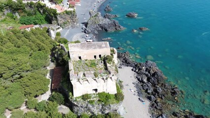 approaching flight aerial view about an ancinent defense tower from Saracen pirates surrounding by green vegetation and spectacular tourque shades colored sea on summer sunlights - Powered by Adobe