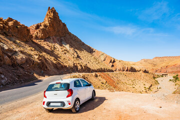 Rental car parking near paved asphalt road in Atlas mountains with high peaks and desert arid...