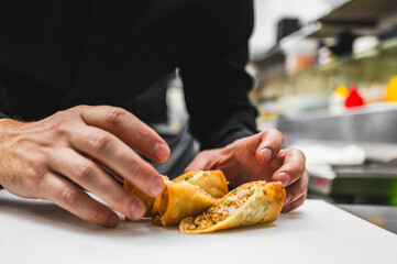 Close-up of hands preparing a spring roll with blurred kitchen background, showcasing fresh ingredients and culinary skills.